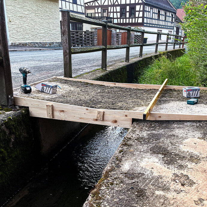 Holzschalung wird über dem Graben montiert und mit Schrauben fixiert, die Ausrichtung wird mit der Wasserwaage kontrolliert.