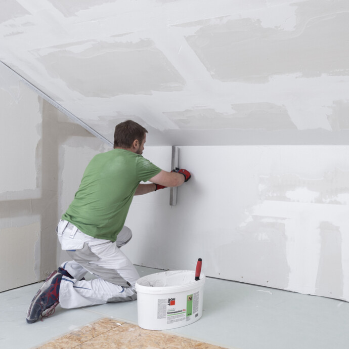 frische, weiße Spachtelmasse mit einem breiten Flächenspachtel an der Wand eben abziehen