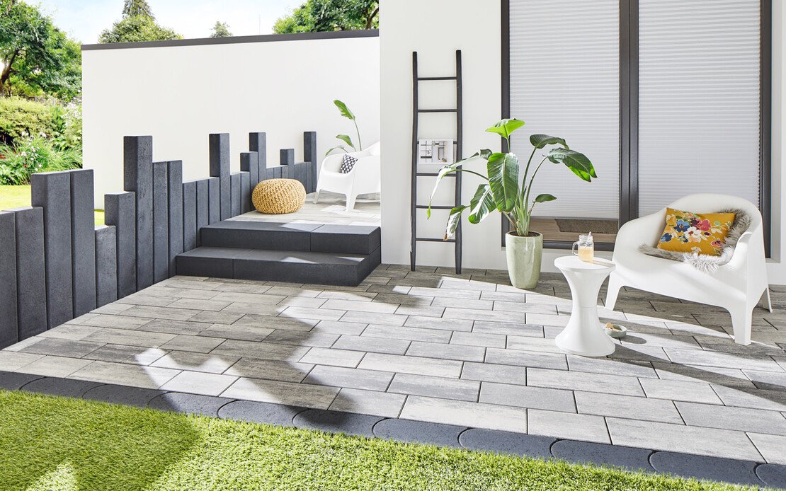 Die moderne Terrasse im Garten ist gestaltet mit hellen Natursteinplatten und anthrazitfarbenen Palisaden.
