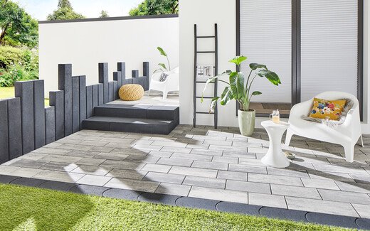 Die moderne Terrasse im Garten ist gestaltet mit hellen Natursteinplatten und anthrazitfarbenen Palisaden.