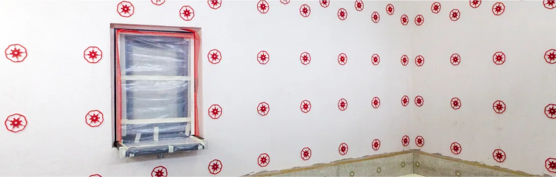 Innenwand mit D&auml;mmstoffbefestigungen, Fensterrahmen abgeklebt; Schritt f&uuml;r Schritt zum effizienten D&auml;mmen und Gestalten von W&auml;nden.