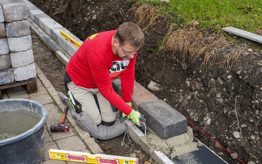 Mit einer Kelle wird überschüssiger Mörtel nach dem Setzen der Steine entfernt.