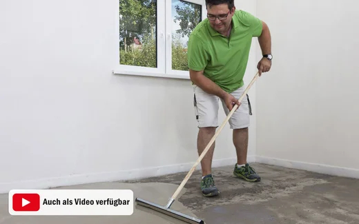 Heimwerker glättet Betonboden mit Abzieher im Innenraum, während Renovierung. Videoanleitung verfügbar.