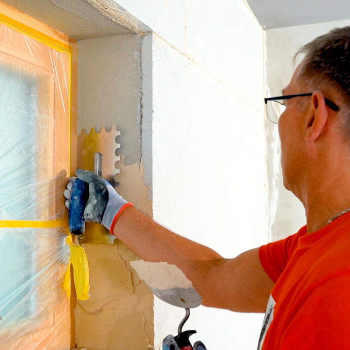 Person trägt den Putz in der Fensterlaibung auf.