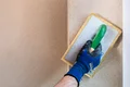 Heimwerker glättet Putz an der Wand mit Reibebrett, um eine gleichmäßige Oberfläche zu schaffen.