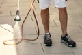 Wasserschlauch wäscht Fliesenbelag auf Terrasse ab, Heimwerker beim Reinigen im Freien, geeignet für Baumit-Projekte.