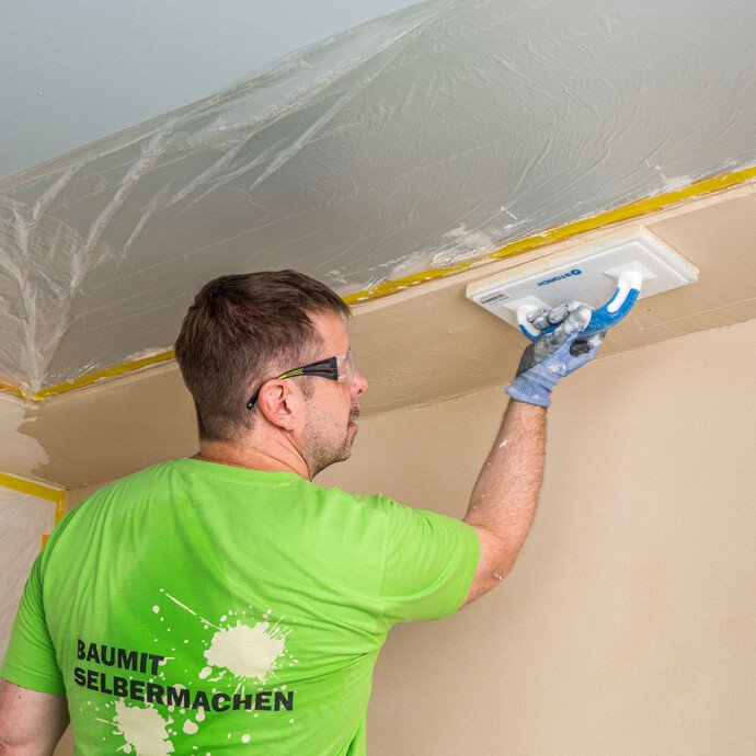 Heimwerker filzt den Dämmkeil im Deckenbereich mit dem Filzbrett ab – Baumit Kalkin Kalkspachtel multifine an schwer zugänglichen Stellen gleichmäßig und sauber filzen, Baumit Selbermachen Anleitung.