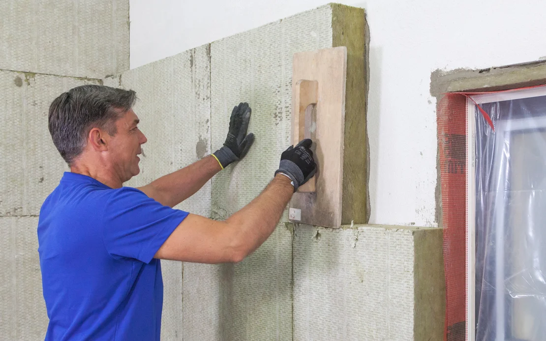 Heimwerker isoliert eine Wand mit Dämmplatten; Schritt-für-Schritt-Anleitung für eine effiziente Wärmedämmung.