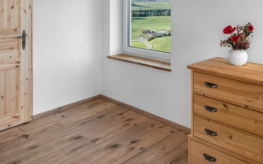 Helles Wohnzimmer mit Holzfußboden, Fenstersitzbank und Holzkommode, ideal für Renovierungsprojekte mit Baumit-Produkten.
