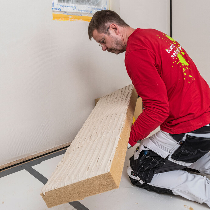 Heimwerker klebt mit Baumit Klebemörtel vollflächig beschichtete Holzfaserdämmplatte kräftig an die Innenwand – Dämmplatte fest andrücken für eine vollflächige und wärmebrückenfreie Verklebung der Innendämmung, Baumit Selbermachen Anleitung.