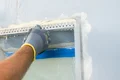Heimwerker verspachtelt Fensterecke mit Kelle und Putzprofil für saubere Kantenabschlüsse.