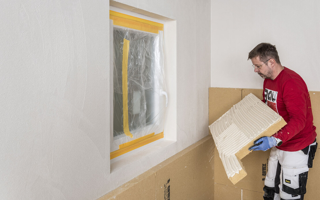 Heimwerker klebt Holzfaserdämmplatte an die Wand. Die Dämmplatte ist in L-Form zugeschnitten. Baumit Selbermachen DIY-Anleitung.