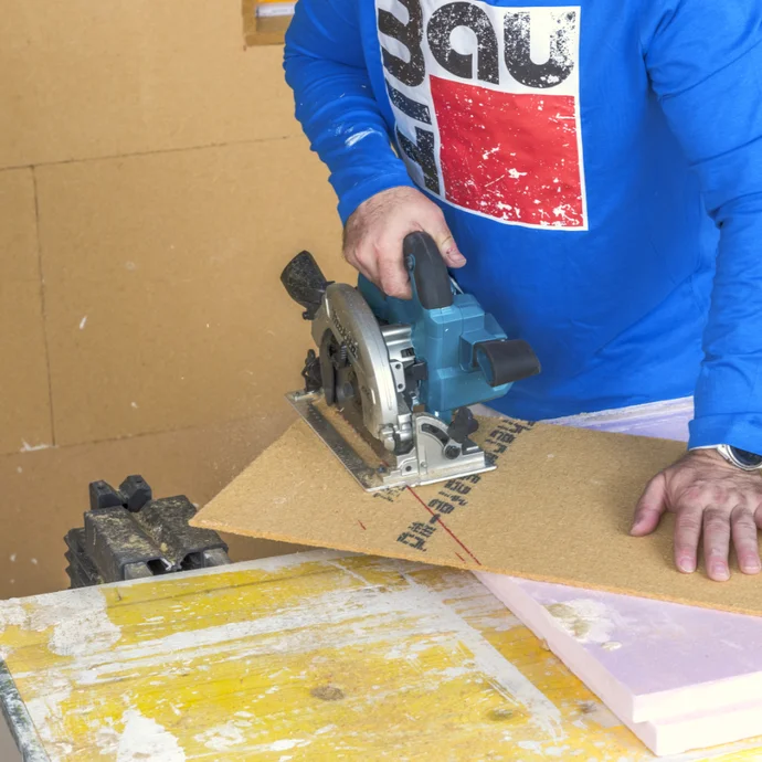 Heimwerker sägt eine Holzplatte mit einer Handkreissäge. Sicherheit und Präzision für DIY-Projekte.