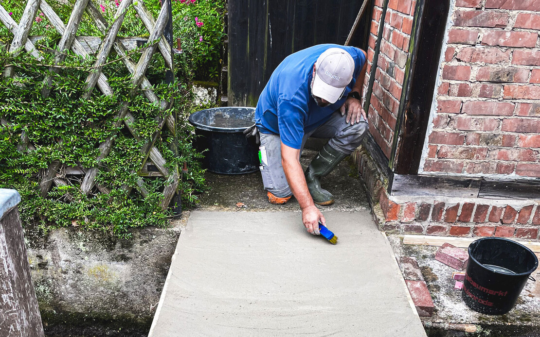 Handwerker raut frische Betonoberfl&auml;che mit B&uuml;rste f&uuml;r bessere Haftung auf.