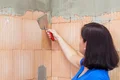 Heimwerkerin verputzt Ziegelwand mit Spachtel; Schritt in einem DIY-Renovierungsprojekt.