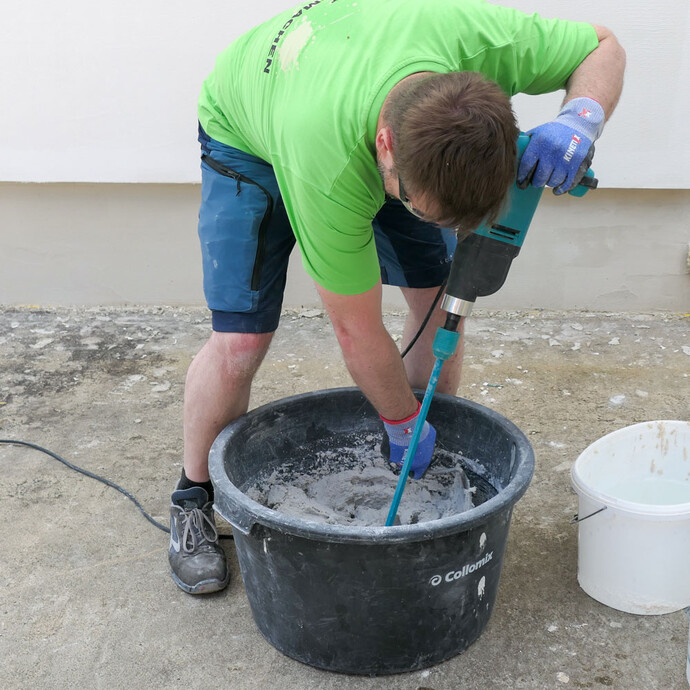 Mann streift trockenes Material am Mörtelkübel ab.