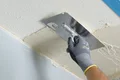Hand verstreicht Putz an Decke mit Kelle, Baumit-Produkte für gleichmäßiges Ergebnis ideal für Heimwerker.