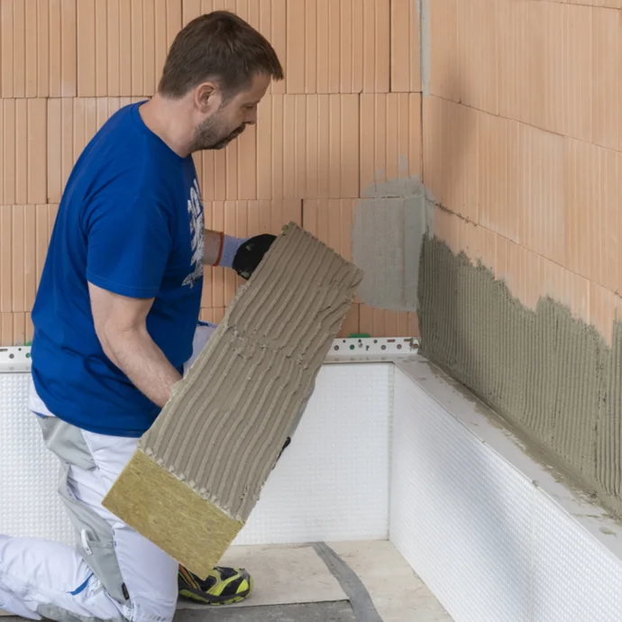 Heimwerker bringt Dämmplatte mit Kleber auf Mauerwerk an, für effektive Wärmedämmung und Energieeinsparung.