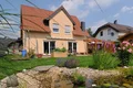 Einfamilienhaus mit verputzter Fassade, Garten und Zierweiher im Vordergrund unter blauem Himmel.