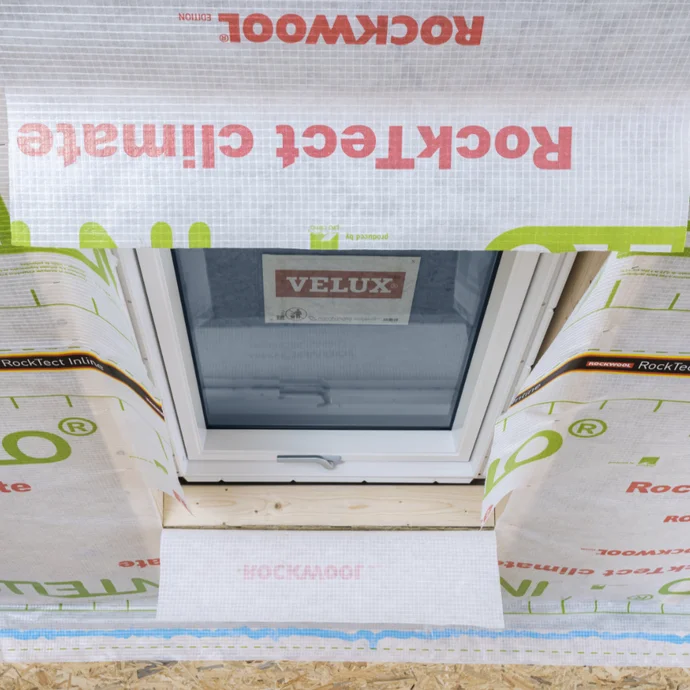 Dachfenster mit Velux-Marke, umgeben von RockTech-Isolationsmaterial, bereit für Dämmungsanleitung auf Baumit-Website.