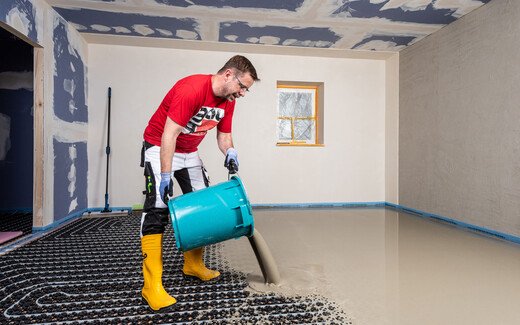 Heimwerker leert den Eimer mit Ausgleichsmasse auf die eingebaute Fußbodenheizung.