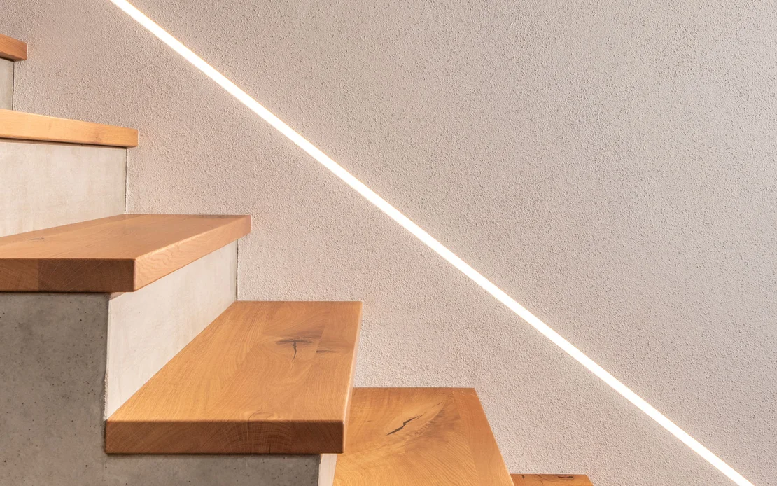 Modernes Treppenhaus mit Beton, indirekter Beleuchtung und dem wohngesunden Baumit Edelputz InStyle Edelwei&szlig;.
