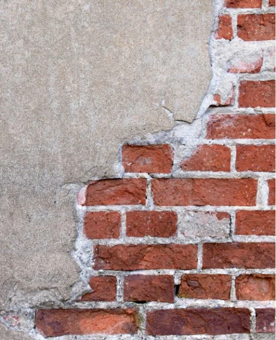 Ziegelwand mit teilweise abgetragenem Putz, ideal für eine Anleitung zur Fassadensanierung und Putzreparatur.
