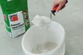 Hand mischt Baumit Innenspachtel in einem Eimer für Renovierungsprojekte.