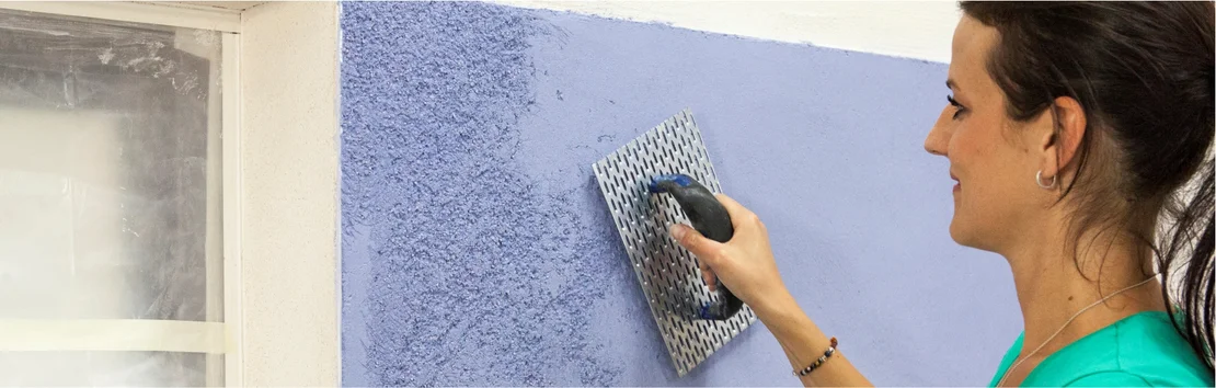 Frau tr&auml;gt blauen Innenputz mit einer Gl&auml;ttkelle auf eine Wand auf, Heimwerkerprojekt in der Renovierung.