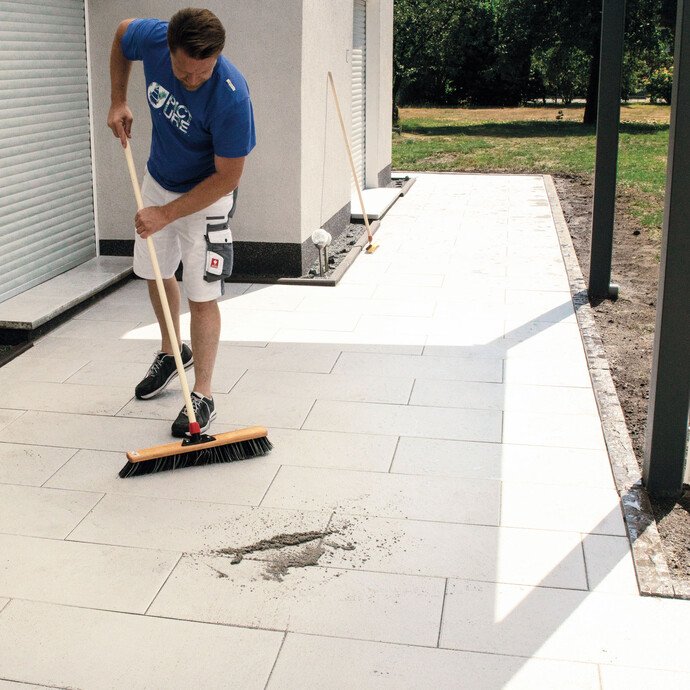 Überflüssiges Fugenmaterial wird mit einem Straßenbesen diagonal zum Fugenverlauf gründlich abgekehrt. 