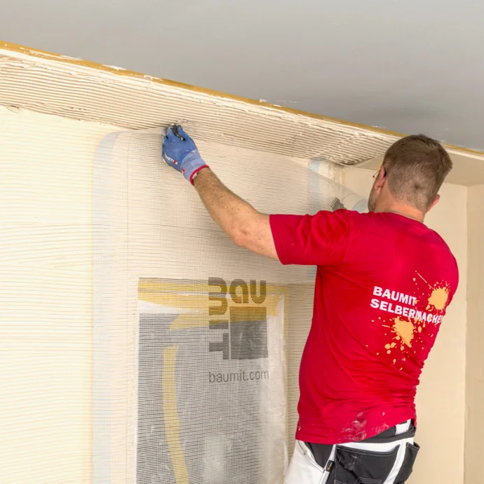 Mann trägt Putz auf Wand auf, Baumit-Logo sichtbar, DIY-Projektanleitung für leichtes Renovieren.