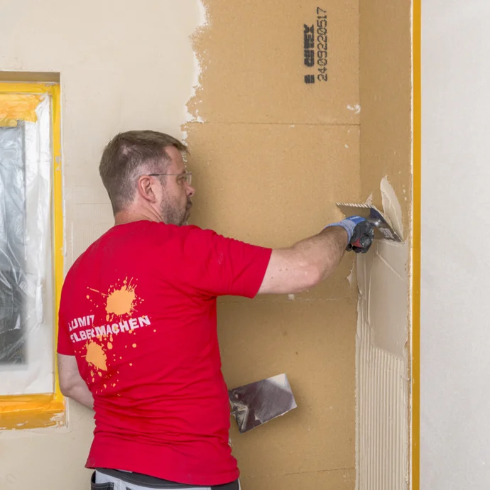 Heimwerker trägt mit Spachtel Masse auf Wand auf; Anleitung zur Wandrenovierung mit Baumit-Produkten.