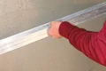 Hand zieht Abziehlatte über frischen Putz an einer Wand, um eine glatte Oberfläche zu erzielen. Schritt in der Wandverarbeitung.