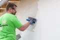 Heimwerker trägt den Münchner Rauputz mit einer Glättkelle auf die Fassade auf.