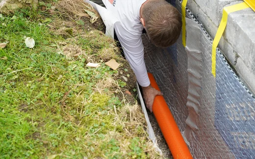 Handwerker verlegt ein Drainagerohr auf dem Filterkies an der Gartenmauer.